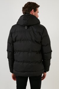 Crna puffa jakna s kapuljačom, koja ima kvadratne dijelove i petlju na izrezu, izrađena od laganog, vodootpornog materijala.