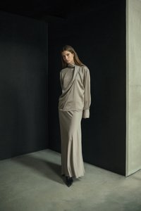 Beige satin top med draperet design, parret med en matchende gulvlange nederdel. Outfitet har lange ærmer og strukturerede skuldre.
