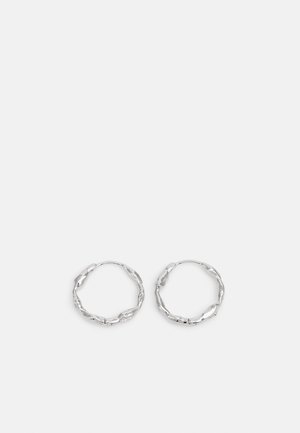 Orecchini a cerchio in argento con una texture ondulata e irregolare. Presentano una forma circolare fine e una finitura riflettente.
