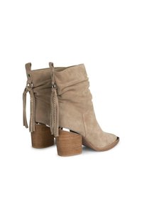 Botines de ante beige con diseño holgado, punta abierta, acentos de borlas, herrajes decorativos y tacón de madera apilada.