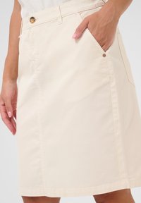Beige katoenen rok met een rechte snit, voorzakken en een knoopsluiting. De stof heeft een gladde structuur met zichtbare stiksels.