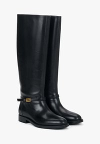 Czarne wysokie skórzane kozaki do kolan o gładkiej fakturze, kanciastym kształcie i złotej ozdobie w postaci klamry na pasku wokół kostki. Płaska podeszwa.