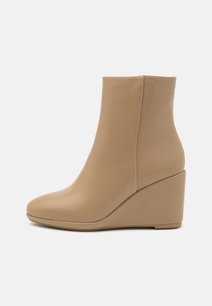Bottine beige en cuir avec une surface lisse, talon compensé, bout rond et couture latérale, présentée sur un fond clair uni.