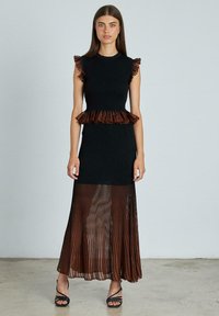 Vestido negro con un top canalé y un acento marrón arrugado en la cintura, que cuenta con una falda de tela transparente plisada y tacones negros destalonados.