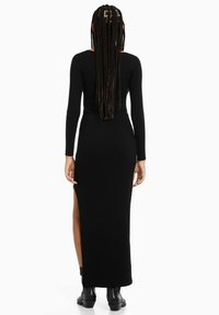 Zwart geribbelde lange mouw jurk met een getailleerde lijfje en een hoge split tot boven de bovenbenen, gemaakt van elastisch materiaal, met een gladde textuur.