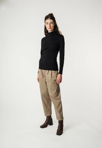 Schwarzes Langarm-Turtleneck-Oberteil, beiges locker sitzendes Hosen und braune Absatz-Stiefeletten, präsentiert vor einem neutralen Hintergrund.