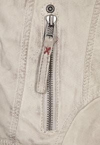 Detail van een witte leren jas met een zilveren rits, leren trekker met rode stiksel en zichtbare stiksels. Getextureerde oppervlakte.