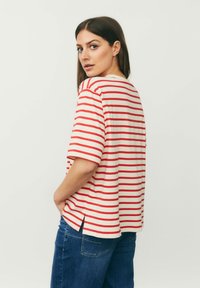 Stribet t-shirt i beige med brede røde striber, korte ærmer, løst fit, sideslids, parret med blå denim jeans.