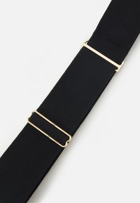 Correa elástica negra con acabado texturizado, que presenta una hebilla de metal en tono dorado para su ajuste. Diseño simple y funcional.