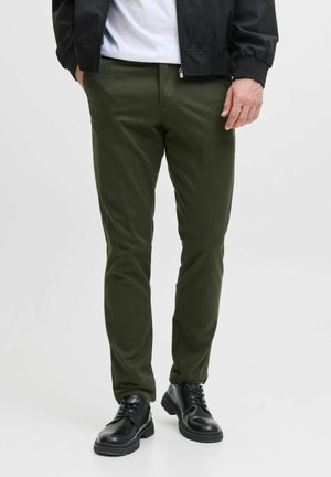 Pantalons vert olive à coupe ajustée, en tissu lisse. Associés à des bottes noires à lacets, dotées d'une semelle texturée et d'accents en chrome.