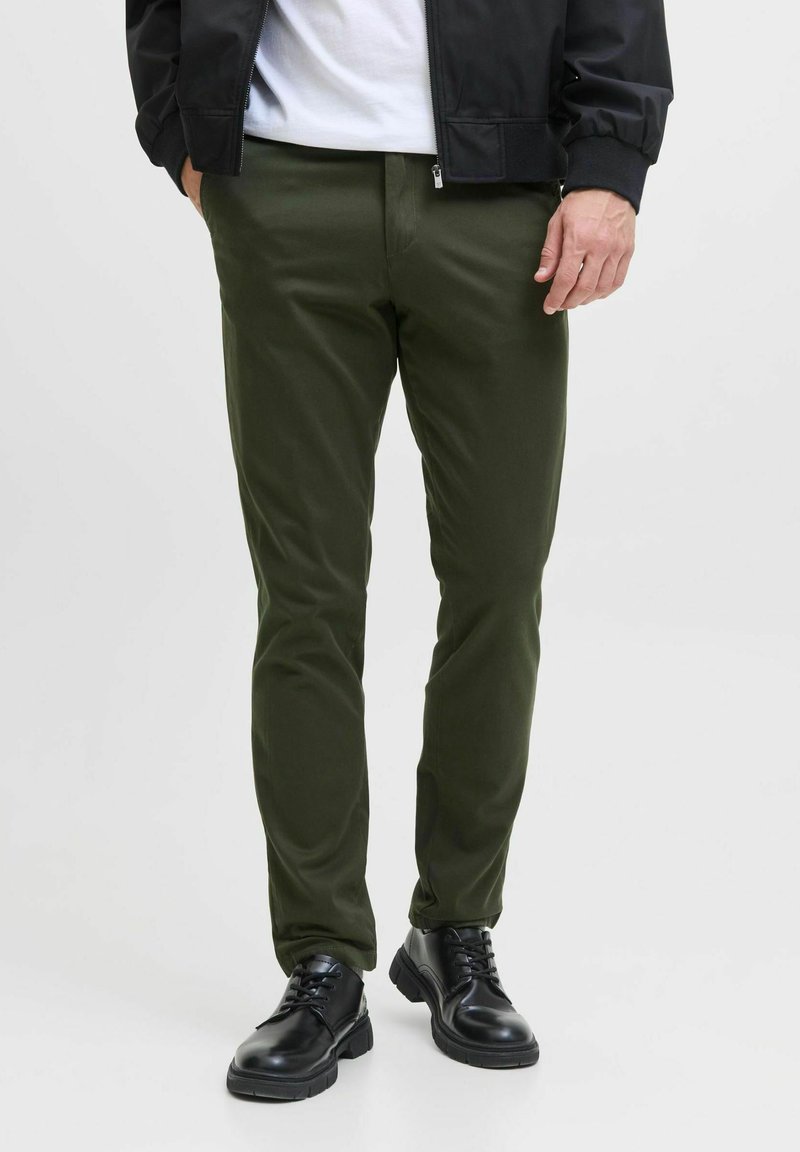 Oliwkowe spodnie o slim fit, wykonane z gładkiego materiału. Połączone z czarnymi sznurowanymi butami, z teksturowaną podeszwą i chromowanymi akcentami.