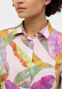 Lightweight, pink blouse featuring a vibrant leaf pattern in green, orange, and purple. Includes a pointed collar and button-up front.