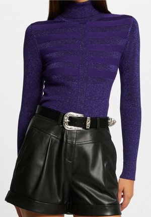 Un modèle portant un haut à manches longues violet avec des rayures subtiles et un col montant, associé à un short en cuir noir et une ceinture décorative.