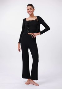 Melns divdaļīgs komplekts ar īsu augšdaļu ar mežģīņu malām un lentu aksesuāriem, kopā ar izplestām biksēm, izgatavots no mīksta auduma.