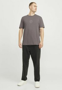 Grå bomulds t-shirt med rund halsudskæring og korte ærmer, der har et diskret solgrafik på brystet. Parret med sorte løstsiddende bukser.
