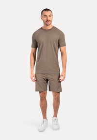 Brązowa koszulka z krótkim rękawem i dopasowane szorty, wykonane z gładkiego materiału. Białe trampki dopełniają stylizację, o prostym, minimalistycznym wzorze.