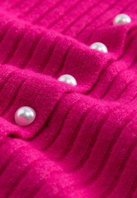 Fuchsia geripptes Strickgewebe mit großen, glänzenden weißen Perlen als Verzierungen, die gleichmäßig an der Vorderseite verteilt sind. Weiche Textur und lebendige Farbe.