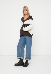 Πλεκτό oversized πουλόβερ σε κρέμα, καφέ και μπλε με γεωμετρικά σχέδια. Συνδυασμένο με τζιν φαρδύ πόδι και μαύρες μπότες με κορδόνια.