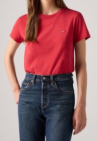 T-shirt en coton rouge avec un col rond et des manches courtes, associé à un jean en denim bleu foncé taille haute avec cinq poches et une braguette à boutons.
