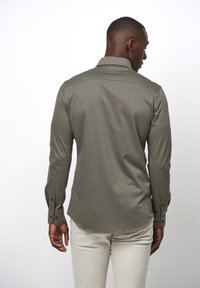 Camicia a maniche lunghe verde oliva con colletto e polsini button-down, orlo curvo e un tessuto liscio e strutturato. Design minimalista.