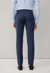 Marineblaue maßgeschneiderte Hose mit strukturierter Webart, ausgestattet mit zwei Gesäßtaschen und slim fit, kombiniert mit schwarzen Lederschuhen.