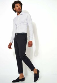 Witte shirt met marineblauwe polka dots, slim fit, gecombineerd met zwarte tapered broek en donkere loafers, met opgerolde mouwen en leren riem.