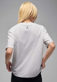 Light grey cotton t-shirt with short sleeves, featuring a small black Jumpman logo on the back near the neckline. Smooth texture.