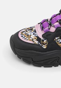 Bout de basket épais avec semelle noire, accents roses, lacets violets et noirs, et tissu à motifs avec motifs baroques dorés et blancs.