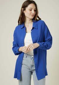 Chemise bleu à manches longues en tissu léger avec un col pointu, à coupe ample, associée à un jean taille haute.