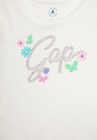 Hvid bomulds t-shirt med "Gap" i glitrende sølv, prydet med farverige blomster og sommerfugle i pink, blå og grøn.