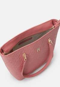 Pink handbag featuring a textured exterior with a geometric pattern, gold hardware accents, and a zip closure at the top.