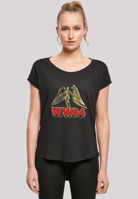 Must have lühikeste varrukatega must T-särk, millel on graafika tiivulise kuju ja "WW84" punases kirjas, pehme tekstuuri ja kumer hem.