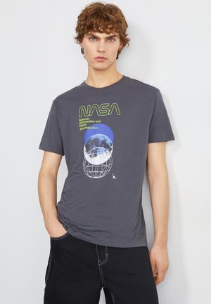Grå T-shirt med NASA-grafik; har blå och vita planetbilder samt grön text. Tillverkad av bomull med korta ärmar och rundad halsringning.