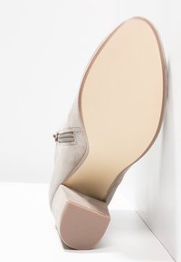 Scarpa alta in suede beige, con tacco affusolato, zip laterale e suola liscia con texture a righe. Colore beige chiaro nel complesso.