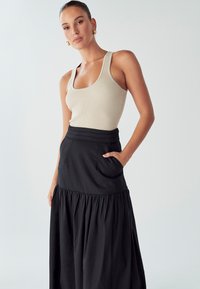 Bež majica s rebrastim vzorcem v kombinaciji z črno krilom, ki ima visok pas, žepe in naguban rob. Gladka tekstura, preprost dizajn.