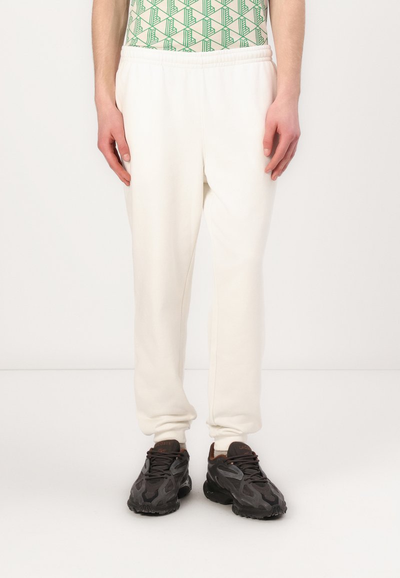 Hvide sweatpants med elastisk talje og manchetter. Blødt, glat stof med en afslappet pasform. Bæres med mørke sneakers, der har tekstureret design.