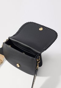 Borsa a tracolla in pelle nera con finitura texturizzata, hardware dorato, bordo intrecciato e tasca interna. Tracolla rinforzata con logo.