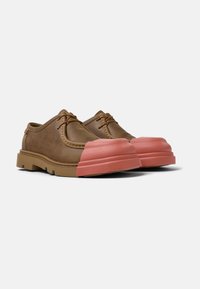 Bruna läderskor med en distinkt rosa gummikappa på tån och beige sula, som visar en blandning av klassiska och moderna designelement.