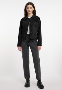 Czarna dżinsowa kurtka z postrzępionymi krawędziami, srebrnymi guzikami i kieszeniami, w połączeniu z szarymi spodniami z wysokim stanem i czarnymi botkami za kostkę.