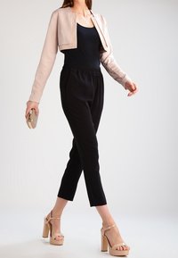 Light beige cropped jacket over a black tank, paired with black tapered pants and beige high-heeled sandals. Accessories include a clutch.