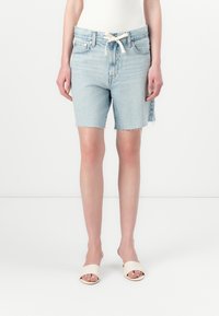 Ljusblå denimshorts med fransiga kanter, hög midja och dragsko. B�ärs med neutrala öppna sandaler.