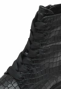 Schwarzer Knöchelstiefel mit strukturiertem, krokogeprägtem Lederobermaterial, rundem Zehenbereich und flachen Schnürsenkeln durch Metallösen.