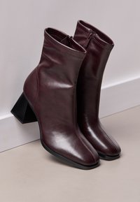 Bottes chelsea en cuir bordeaux avec un bout arrondi élégant, des détails de couture et un talon bloc géométrique. Fermeture éclair à l'arrière.