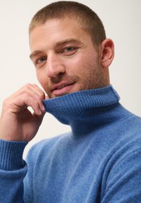 Modrý rolák vyrobený z měkké, texturované tkaniny. Vyznačuje se ribbed výstřihem a manžetami, má volný střih a jemné zabarvení po celém povrchu.