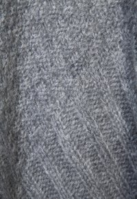 Grå stickad tyg med en texturerad, diagonal mönstring. Det ulliga materialet har ett mjukt utseende som ger djup och värme åt designen.