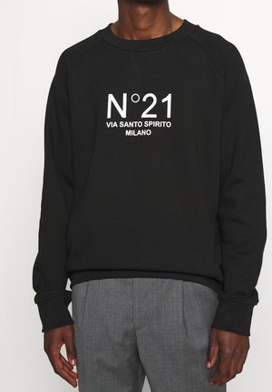 Felpa nera con testo bianco che legge "N°21 VIA SANTO SPIRITO MILANO." Presenta un collo rotondo e polsini a coste. Abbinata a pantaloni grigi.