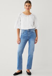 White blouse with eyelet pattern and gathered neckline, paired with light blue straight-leg jeans. Black flats complete the look.