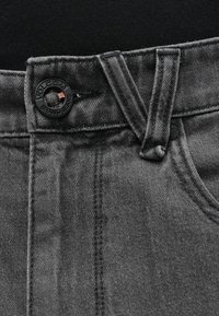 Μαύρο τζιν από τζιν ύφασμα με κλείσιμο με κουμπί που φέρει λογότυπο, ορατές ραφές και υφή υφάσματος με ανάγλυφη επιφάνεια. Κλασικός σχεδιασμός με πέντε τσέπες.