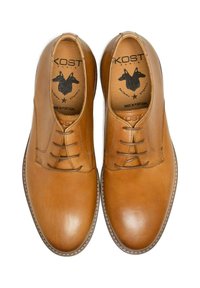 Chaussures en cuir tan avec un bout arrondi, dotées de cinq œillets et d'une trépointe cousue. La semelle intérieure présente une marque et un design graphique.