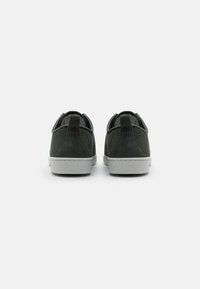 Dunkelgrüne Wildledersneaker mit einer flachen grauen Gummisohle, gepolstertem Schaft und kontrastierenden grauen Akzenten an den Kanten. Rückansicht.